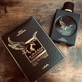 Lattafa Malik Al Tayoor Concentrated 100ml — A black perfume box with gold eagle emblem and text sits next to a black perfume bottle with a gold eagle emblem on a wooden surface. | Lattafa Malik Al Tayoor Concentrated 100ml — Kotak minyak wangi hitam dengan lambang helang emas dan teks terletak di sebelah botol minyak