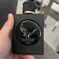 Lattafa Malik Al Tayoor Concentrated — A black perfume bottle with a gold eagle emblem and Arabic text, held in a hand. | Botol minyak wangi hitam dengan lambang helang emas dan teks Arab, dipegang di tangan.