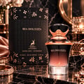 Maison Alhambra Mia Dolcezza — Black box with rose gold floral accents and deer logo next to a black and rose gold gradient perfume bottle with a faceted black cap, set on a marble surface with jewelry.