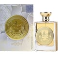 Ard Al Zaafaran Mithqal 100ml — A clear glass perfume bottle with gold liquid and a circular gold emblem featuring winged creatures and Arabic script, next to its matching white and gold patterned box with a similar emblem. | Ard Al Zaafaran Mithqal 100ml — Botol minyak wangi kaca jernih dengan cecair emas dan lambang