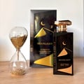 Gulf Orchid Moonlight Eau De Parfum 100ml by Gulf Orchid — A black perfume bottle with gold desert dunes and crescent moon design stands next to a clear hourglass filled with gold glitter. The perfume box is in the background. | Gulf Orchid Moonlight Eau De Parfum 100ml by Gulf Orchid — Botol minyak wangi hitam dengan
