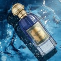 Al Wataniah Muheeb Perfume Man by Al Wataniah 100ml — A blue glass perfume bottle with a gold cap is submerged in water with splashes and bubbles. | Al Wataniah Muheeb Perfume Man by Al Wataniah 100ml — Botol kaca biru dengan penutup emas tenggelam dalam air dengan percikan dan buih.