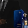 Al Wataniah Muheeb Perfume Man by Al Wataniah 100ml — A man in a dark suit stands to the left, with a blue perfume box and bottle on the right. | Al Wataniah Muheeb Perfume Man by Al Wataniah 100ml — Seorang lelaki berbaju gelap berdiri di sebelah kiri, dengan kotak dan botol minyak wangi biru di sebelah kanan.