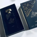 Lattafa Musk Al Aroos by Lattafa 80ml EDP — A dark blue perfume bottle with a gold cap sits inside an open dark blue box, with the matching outer box to the right, featuring ornate gold cutouts and Arabic script. | Lattafa Musk Al Aroos by Lattafa 80ml EDP — Botol minyak wangi biru gelap dengan penutup emas terletak