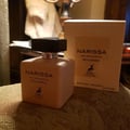 Maison Alhambra Narissa Poudree 100ml — A square-shaped, pale peach perfume bottle with a black cap sits on a textured surface next to its matching pale peach box. | Maison Alhambra Narissa Poudree 100ml — Botol minyak wangi berbentuk segi empat, berwarna pic pucat dengan penutup hitam duduk di atas permukaan