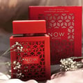 Rave Now Rouge Perfume EDP 100ml by RAVE — A red perfume bottle with a geometric cut-out design and a red cap, placed next to its red box with a similar geometric pattern. Delicate white flowers adorn the foreground. | Rave Now Rouge Perfume EDP 100ml by RAVE — Botol minyak wangi merah dengan reka bentuk potongan