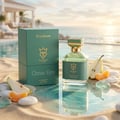 Bujairami Ocean Eyes 100ml Extrait — Green box and glass bottle with gold accents on sand, next to sliced pear and mandarin segments, with a blurred resort pool and ocean background.