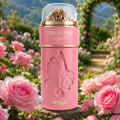 Zimaya Ode to Rose Royale Eau De Parfum 100ml by Zimaya — A pink perfume bottle with rose embossing sits in a garden filled with pink roses, with a blurred background of greenery and a stone archway. | Zimaya Ode to Rose Royale Eau De Parfum 100ml by Zimaya — Botol minyak wangi merah jambu dengan ukiran mawar