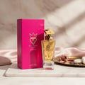 Bujairami Only Ever by Bujairami 100ml EDP — Gold-capped glass perfume bottle next to a vibrant pink textured box, set on a marble surface with silk fabric and decorative dried flowers.