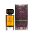 Ard Al Zaafaran Oud Al Turas 100ml — A clear glass perfume bottle with amber liquid and a gold cap sits next to its matching purple and gold ornate box on a white background. | Ard Al Zaafaran Oud Al Turas 100ml — Botol minyak wangi kaca jernih dengan cecair ambar dan penutup emas terletak di sebelah kotak perhiasan