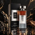 Ard Al Zaafaran Oud Romancea Fakhama — Black ribbed box and fluted glass perfume bottle with amber liquid, set against dark, textured rocks and rippling water.