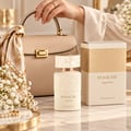 Khadlaj Panache Angel Dust — Beige handbag with gold clasp, silk scarf, perfume bottle with embossed design, and product box on marble surface with white flowers.
