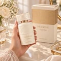 Khadlaj Panache Angel Dust — Woman's hand holding a white and gold embossed perfume bottle, with the matching box in the background, surrounded by white roses and decorative items.