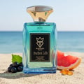Bujairami Perfect Life Eau de Parfum 100ml — Blue glass perfume bottle with gold cap on a sandy beach with ocean background, featuring grapefruit slice and blackcurrants.