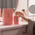 Afnan 9 AM – Pour Femme by Afnan Perfumes – 100 ml for Women — A hand holds a clear glass perfume bottle with a gold cap, featuring a pink label with '9 am pour femme' text, next to its matching pink box on a pink vanity.