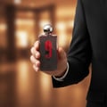 Afnan 9 PM Rebel by Afnan EDP 100 ml Men — Man in black suit holding a clear glass perfume bottle with red label and silver