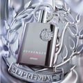 Afnan Supremacy Not Only Intense Extrait 100ml — Botol wangian perak berkilat dengan logo bulat di tengah, diletakkan di atas perhiasan perak berbentuk daun dan reben bertulis 'SUPREMACY'.