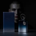Afnan Supremacy Incense — A dark, moody shot of a blue gradient perfume bottle and its box, with a man's blurred face in the