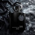 Afnan Supremacy Noir by Afnan 100ml EDP Men — Botol wangian hitam legam dengan penutup bulat, diletakkan di atas latar belakang bertekstur gelap dan berkilauan seperti batu pecah dan fabrik satin.