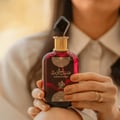 Al Wataniah Sabah Al Ward — Woman's hands hold a dark red perfume bottle with gold accents and a faceted black cap.