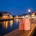 Ard Al Zaafaran Ahubbak Love In Paris EDP 100ml Zaafaran — Pink perfume bottle and box on wooden railing by canal at dusk.