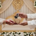 Ard Al Zaafaran Daar Al Haneen Women — Hands exchanging a decorative gold perfume bottle with black ribbon and rose detail.