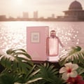 Ard Al Zaafaran Heibah by Ard Al Zaafaran 100ml For Her — Botol wangian kaca jernih berisi cecair merah jambu, diletakkan di sebelah kotak merah jambu yang sepadan. Latar belakang air berkilauan dengan bangunan di kejauhan. Dikelilingi daun tropika dan bunga.