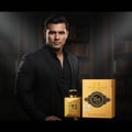 Ard Al Zaafaran Oud 24 Hours Majestic 100ml EDP Man – A man in a black suit stands next to a gold perfume bottle and box.