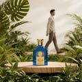 Ard Al Zaafaran Satwa — Blue perfume bottle on wooden stand surrounded by lush green foliage, man walking in background