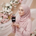 Ard Al Zaafaran Zahoor Francee — Woman in pink hijab holding a perfume bottle with a black band and Arabic script.
