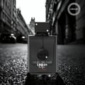 Armaf Club De Nuit Urban Elixir — Black perfume bottle on a wet, cobblestone street with blurred city buildings and cars in