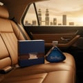 Armaf Tres Nuit — Blue fragrance box and triangular bottle on tan leather car seat with city skyline at sunset