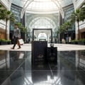 Asdaaf Shaghaf Man by Asdaaf (Lattafa) – 100 ml for Men. A man walks past a display of the perfume box and bottle in a modern mall atrium with palm trees.