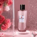 Grandeur Glitz Glam by Grandeur Elite 100 ml for Women — A tall, glitter-infused pink perfume bottle with a gold-accented black cap, displayed on a clear acrylic stand. Pink roses with water droplets are visible in a glass container to the left.
