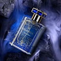 Grandeur Calabria Cerulean by Grandeur Elite 50ml for Him — Blue glass perfume bottle with gold flecks and ornate blue gem cap, set against dark rocks and wispy blue smoke.