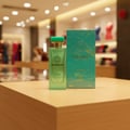 Grandeur Avenue London 100ml EDP – Green glass perfume bottle with gold accents and a teal box, displayed on a wooden surface with a blurred retail background.