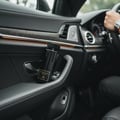 Grandeur Instinct Noir by Grandeur 100ml For Men — Black perfume bottle with gold label resting on the leather door panel of a luxury car.