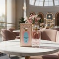 Grandeur Perfectly Pink by Grandeur Woman 100ml — Pink perfume bottle and its box displayed on a marble table in a luxurious cafe setting with floral arrangements.