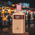 Grandeur Tribal Gold Man by Grandeur 100ml EDP Men — Gold bottle with rose gold textured cap, dark brown label with "TRIBAL GOLD" text, and Grandeur Elite logo, set against a blurred night market background with bokeh lights.