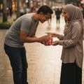 Grandeur Opulent Bloom Red by Grandeur Elite 100 ml for Women — A man in a grey t-shirt and jeans offers a red perfume bottle with a gold cap to a woman wearing a hijab.