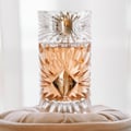 Gulf Orchid Sweet Heaven by Gulf Orchid 100ml EDP Unisex — Close-up of a clear, faceted glass perfume bottle with rose-gold liquid, featuring a diamond-shaped gold label with 'SWEET HEAVEN' text, resting on a soft, beige cushion.