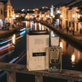 Lattafa Ana Abiyedh by Lattafa 60ml EDP Unisex — Perfume bottle and box on a railing at night with a canal and illuminated