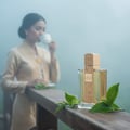 Lattafa Angham by Lattafa EDP 100ml Women — Woman in traditional attire sips tea near a perfume bottle and tea leaves on a