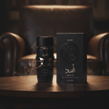 Lattafa Asad Elixir Lattafa 100ml for Men — Botol wangian hitam dengan reka bentuk emas dan kotak hitam di atas meja kayu, dengan kerusi kulit di latar belakang dan asap.