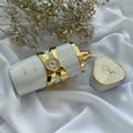 Lattafa Yara Moi by Lattafa 100ml EDP Women — White perfume bottle with gold accents and Arabic script, lying on white fabric next to its triangular gold-rimmed cap and dried flowers.