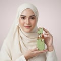 Lattafa Eclaire Pistache by Lattafa 100ml EDP Unisex — Woman in cream hijab holding green and gold perfume bottle.