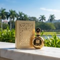 Lattafa Fakhar Extrait — Gold perfume bottle and box on marble ledge with palm trees and water background.