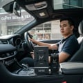 Lattafa Hayaati Men by Lattafa Perfumes100ml EDP — Man in car holding steering wheel, with Hayaati perfume bottle and box on center console.