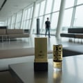 Lattafa Jasoor oleh Lattafa Perfumes 100 ml Unisex — Kotak dan botol minyak wangi emas dengan kaligrafi Arab di atas meja gelap di ruang menunggu lapangan terbang moden.