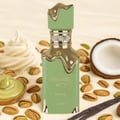 Lattafa Eclaire Pistache — Green perfume bottle with gold accents, surrounded by pistachios, coconut half, and vanilla bean.
